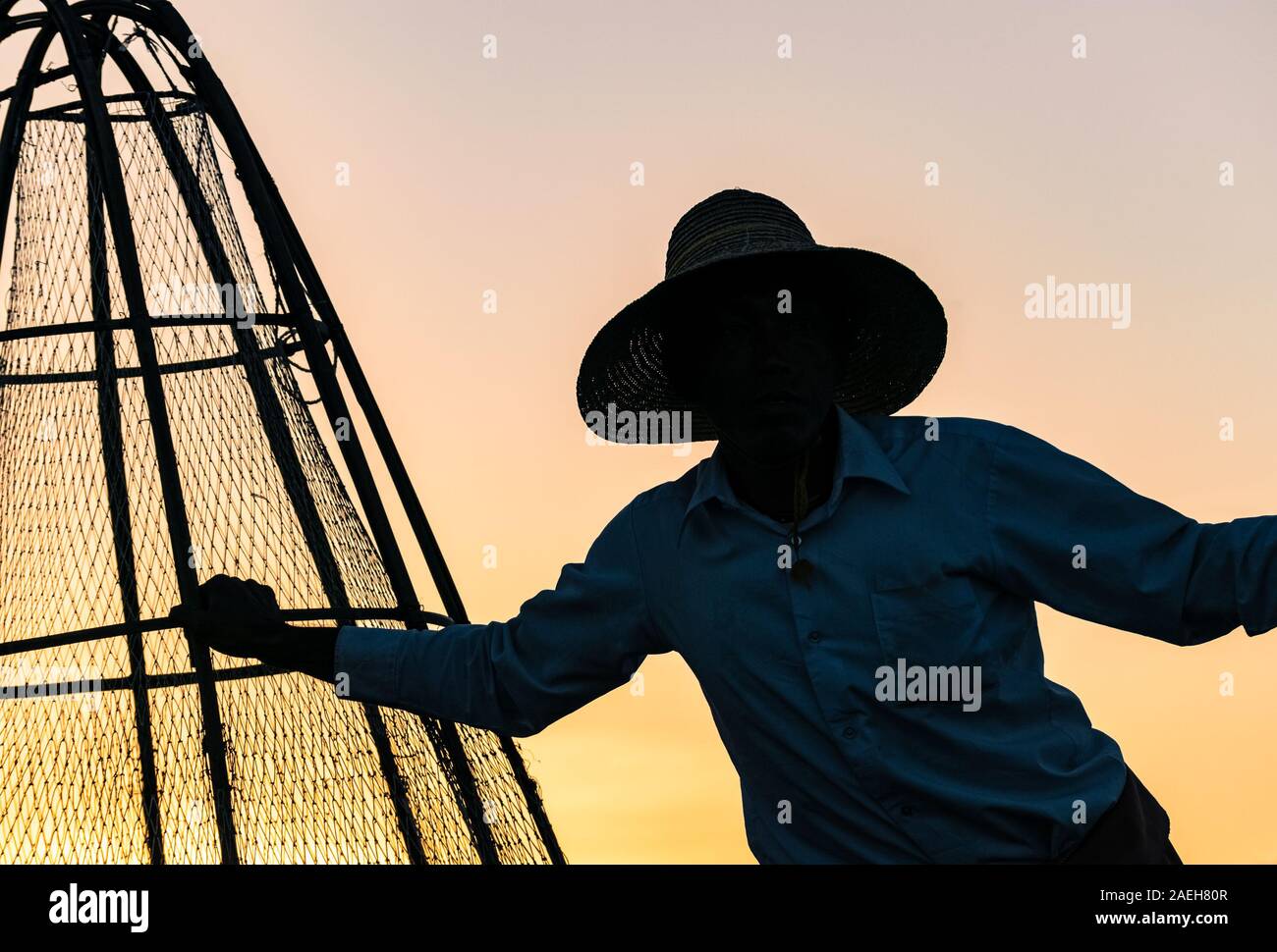 Pescatore birmano in posa per i turisti al tramonto al Lago Inle. Le tradizionali reti da pesca ha conseguito non sono più utilizzate per la pesca da Intha persone. Foto Stock