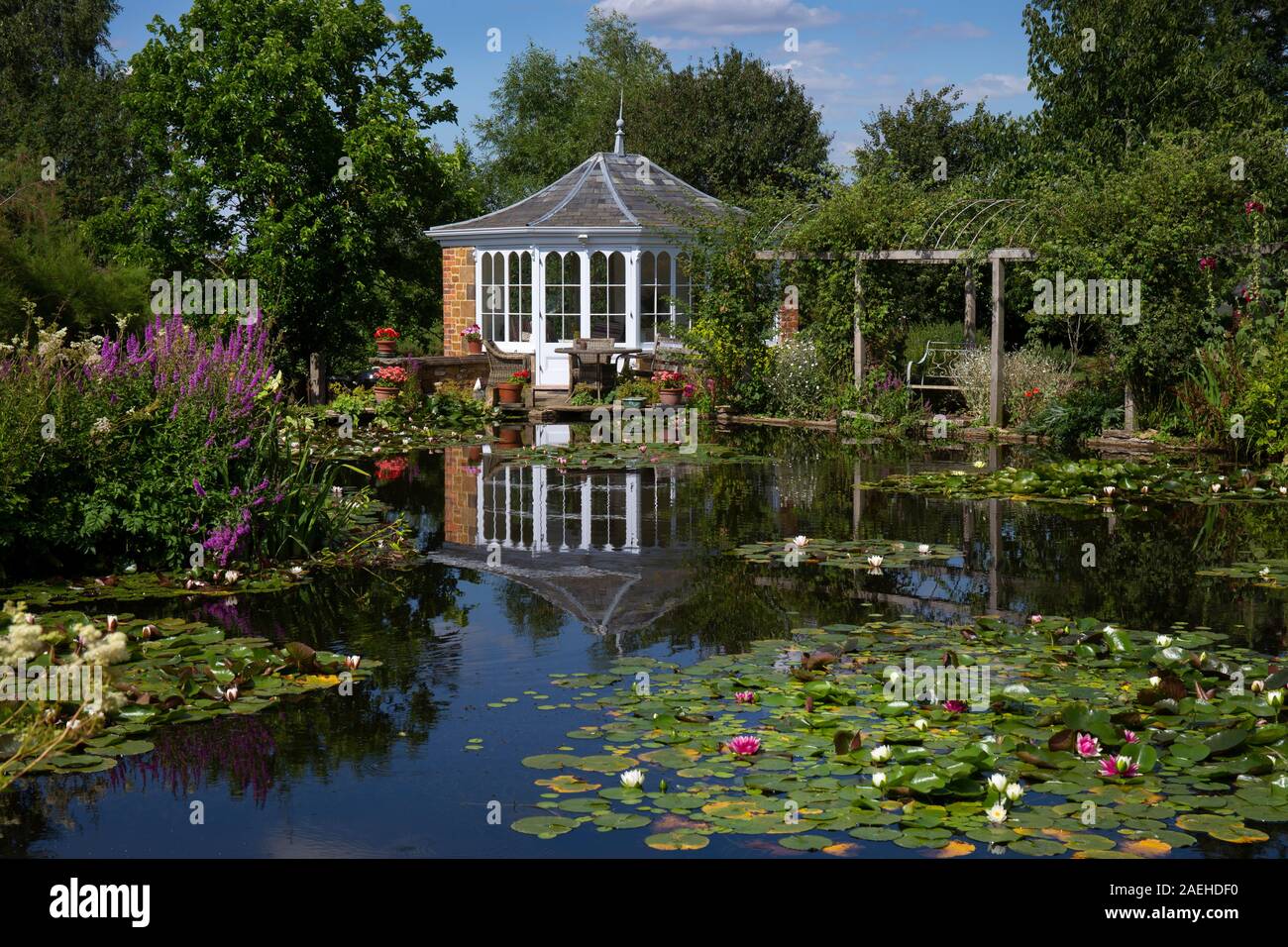 Garden summerhouse guardando oltre stagno ornamentale con acqua lillies nel giardino inglese,Inghilterra Foto Stock