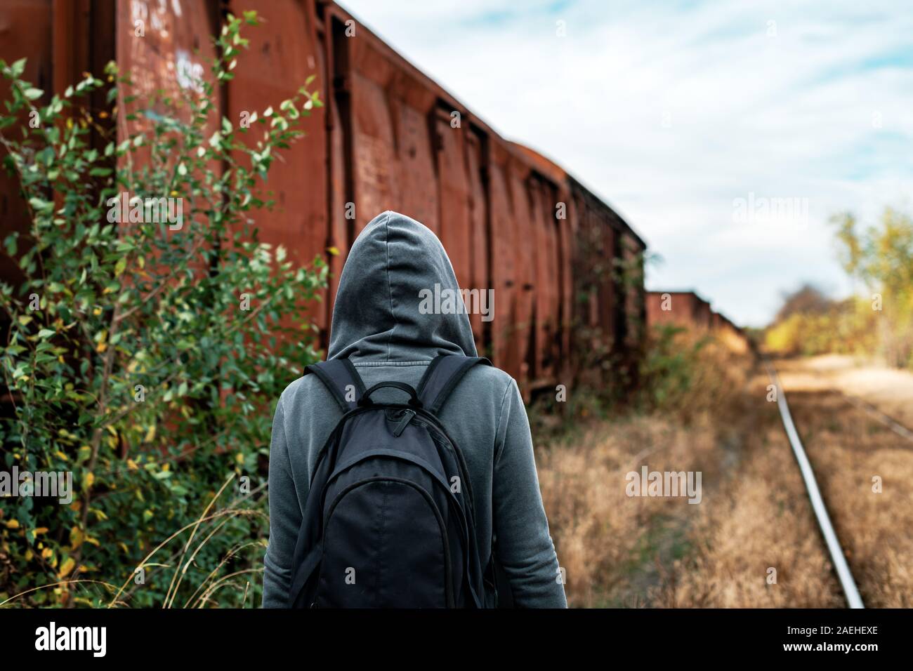 Donna senzatetto con zaino allontanarsi da tutto e da tutti, vista posteriore delle donne in cammino tra abbandonato i vagoni del treno e ferrovia obsoleti via Foto Stock