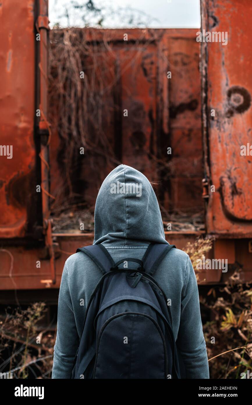 Donna senzatetto con zaino allontanarsi da tutto e da tutti, vista posteriore delle donne in cammino tra abbandonato i vagoni del treno e ferrovia obsoleti via Foto Stock