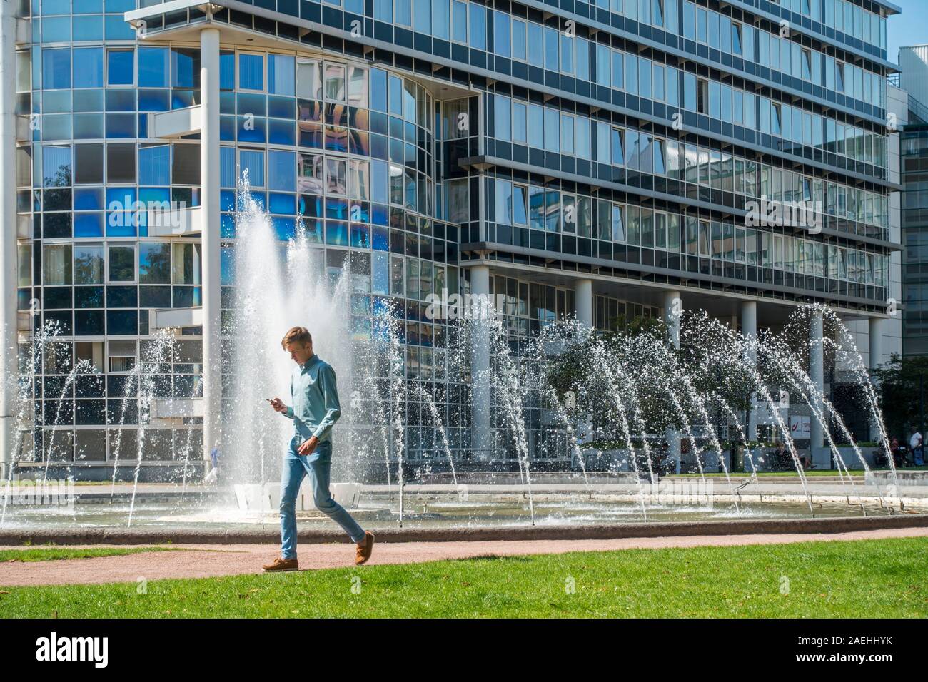 Uomo che cammina durante la lettura di smartphone nella parte anteriore della fontana nel re Albert Park, il parco della città nel distretto del Sud a Gand, Fiandre Orientali, Belgio Foto Stock