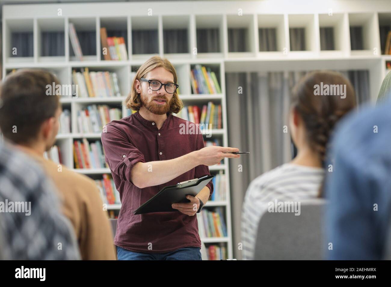 Giovane insegnante holding relazione e spiegare il nuovo materiale per gli studenti durante una lezione nella libreria Foto Stock