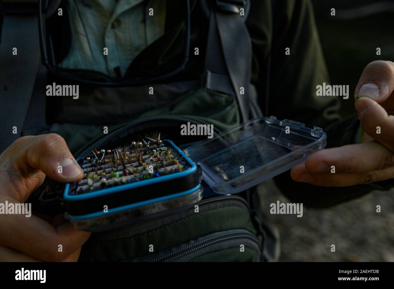 Un pescatore in possesso di una scatola piena di piccole mosche Foto Stock