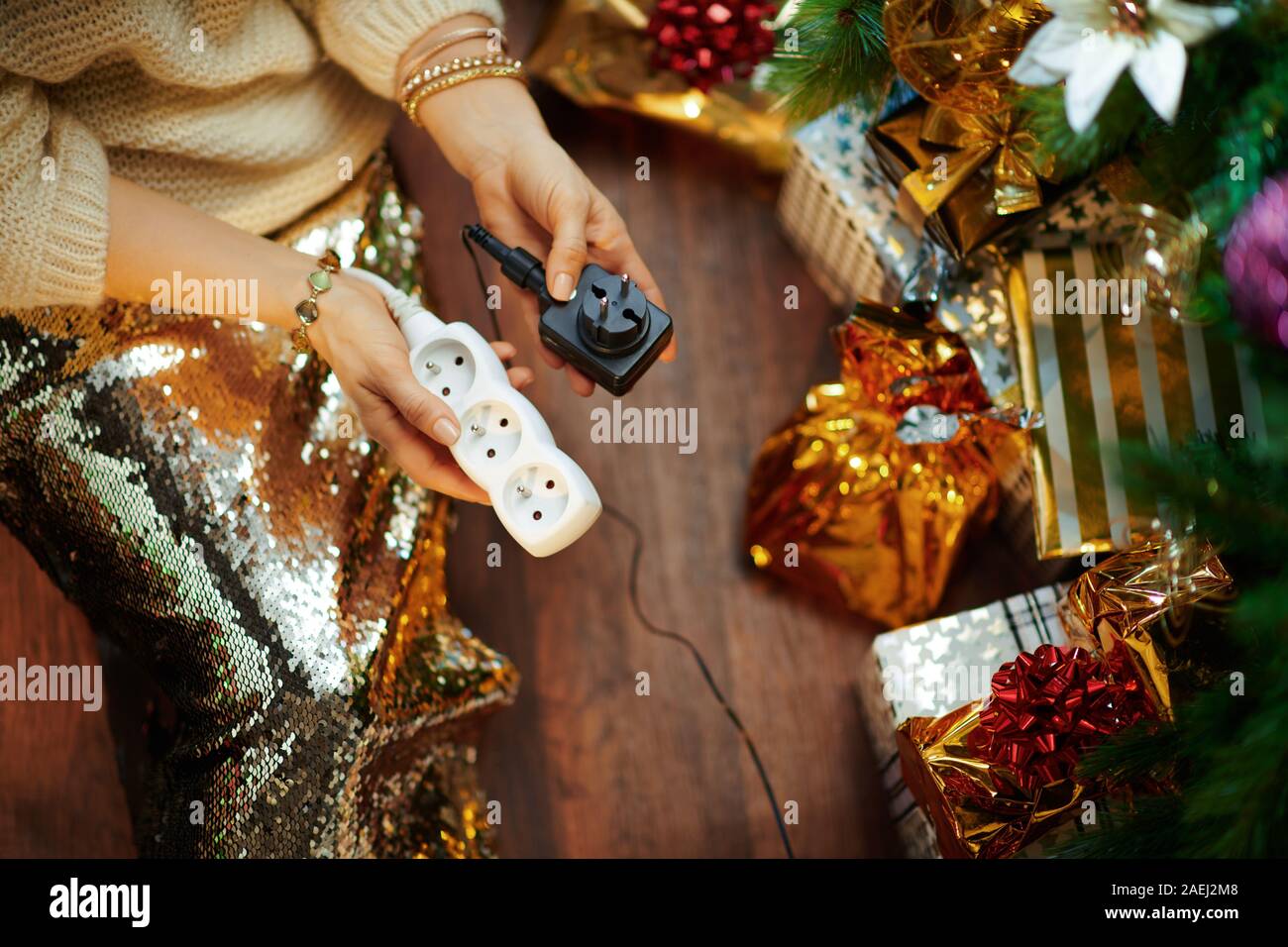 Dubitando eleganti donna in oro zecchino gonna e maglione bianco con cavo da garland elettrica e cavo di estensione avente le preoccupazioni per la sicurezza sotto decorat Foto Stock