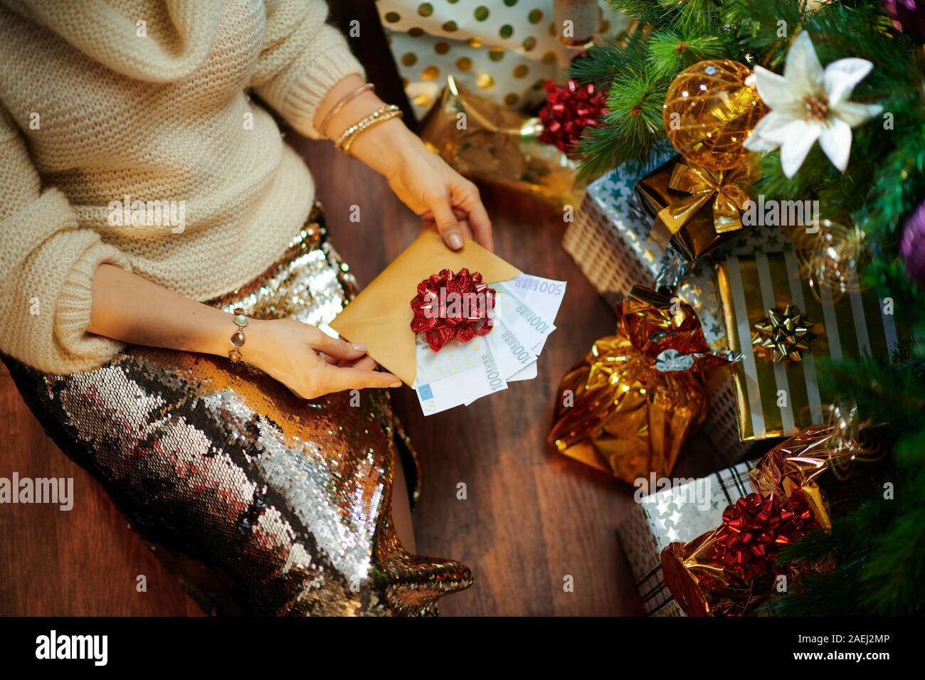 Primo piano sul moderno 40 enne casalinga in oro zecchino gonna e maglione  bianco sotto albero di Natale decorato nei pressi di caselle presente  guardando il Natale Foto stock - Alamy
