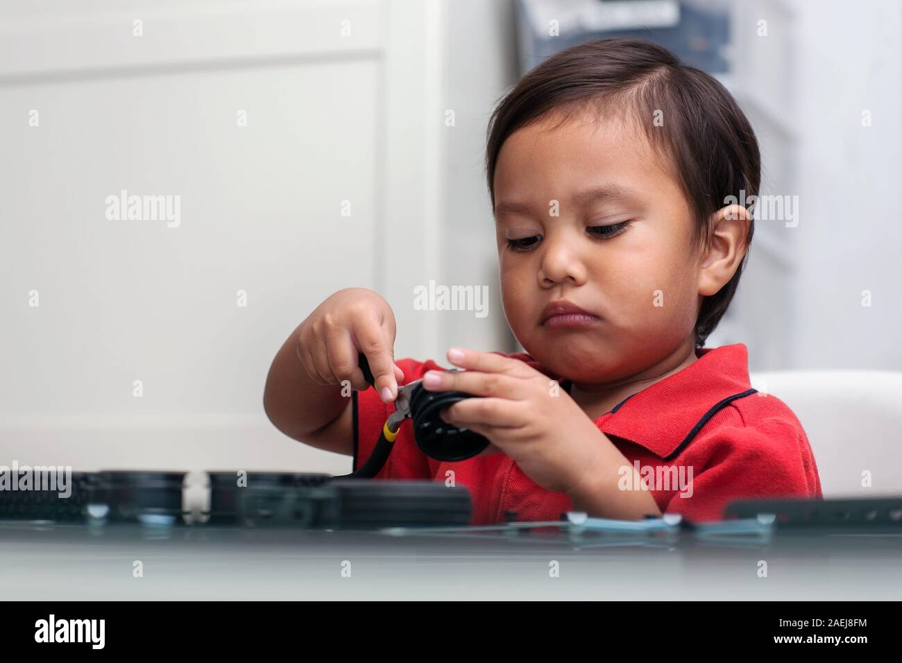 Una smart latino ragazzo con un intenso sguardo attento è imparare a conoscere gli strumenti mentre si sta giocando con parti di giocattoli e tenendo un ago naso plyer nella sua mano. Foto Stock
