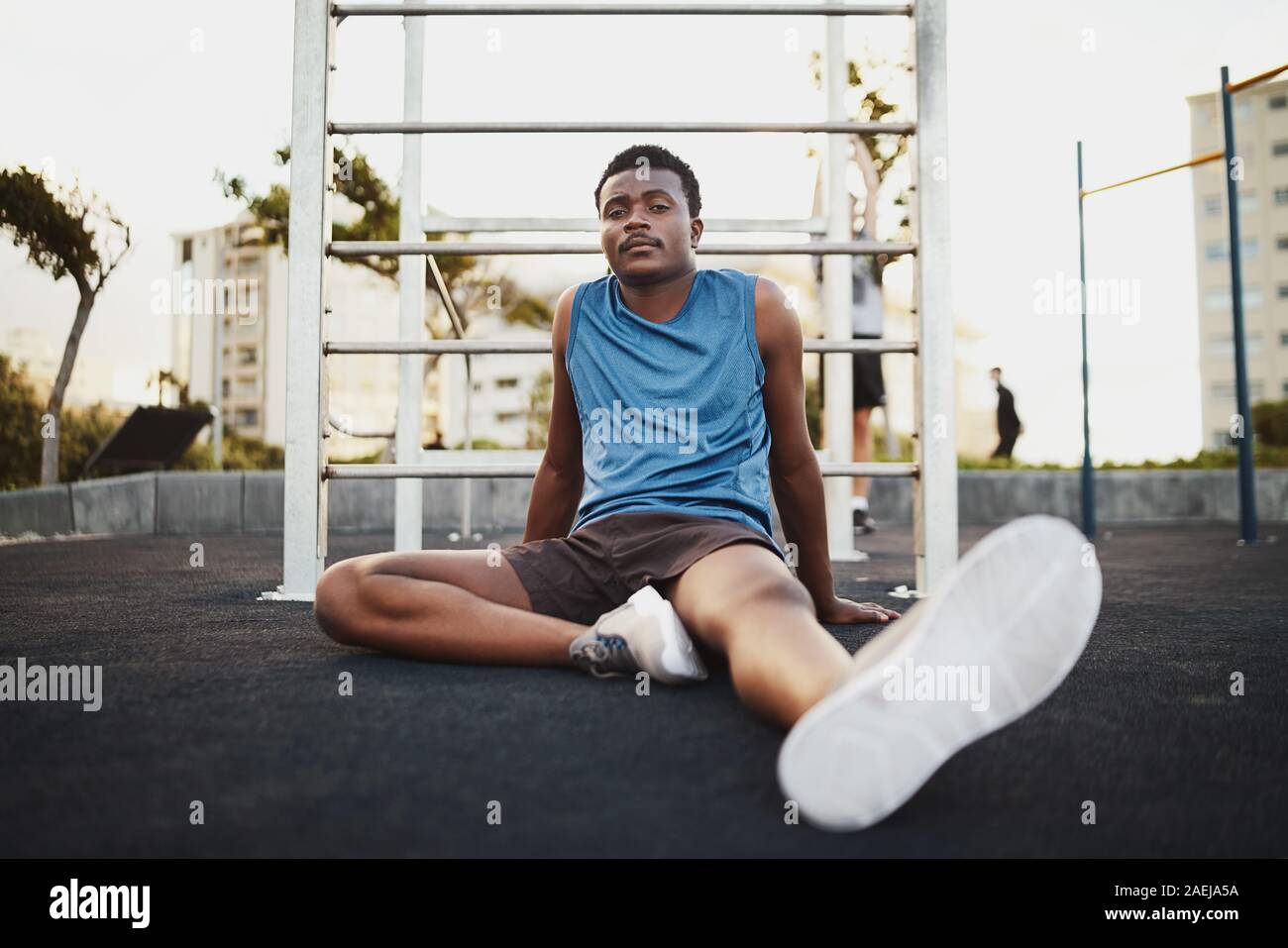 Ritratto di una stanca fitness americano africano giovane uomo seduto su outdoor parco pubblico terra tenendo il resto dopo formazione di allenamento Foto Stock