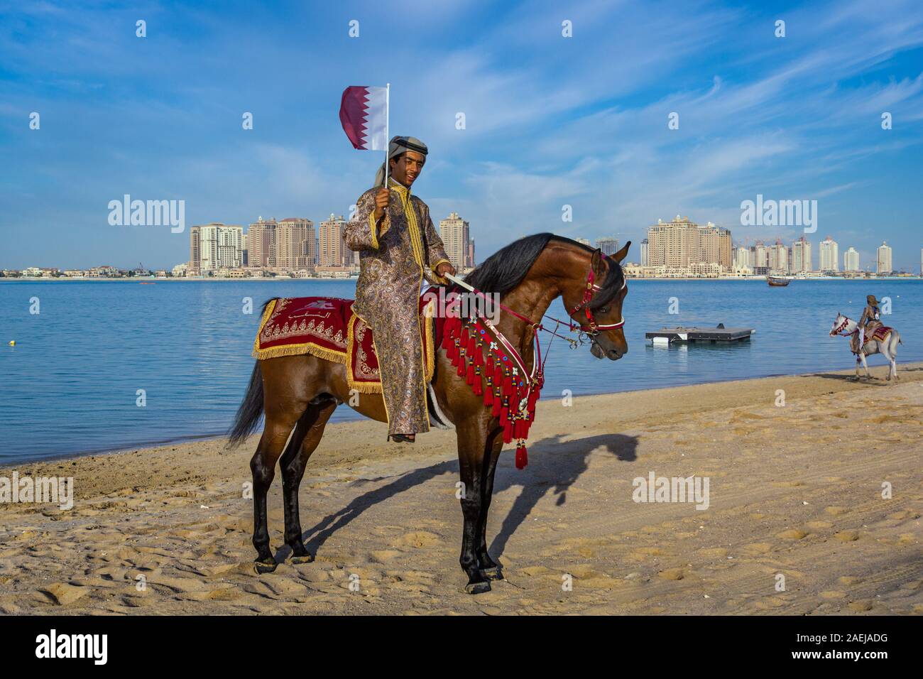 Un uomo Qatar equitazione e portare bandiera Qatar in Katara spiaggia Doha, Qatar celebrazione del Qatar National Day Foto Stock