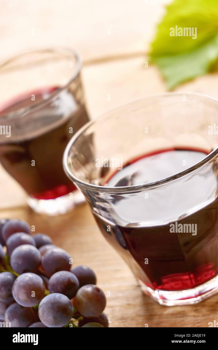 Informale due bicchieri di vino senza il piede su una tabella riempita con il vino rosso, blu uva e un verde foglia di uva. Verticale angolo olandese con il fuoco selettivo. Foto Stock