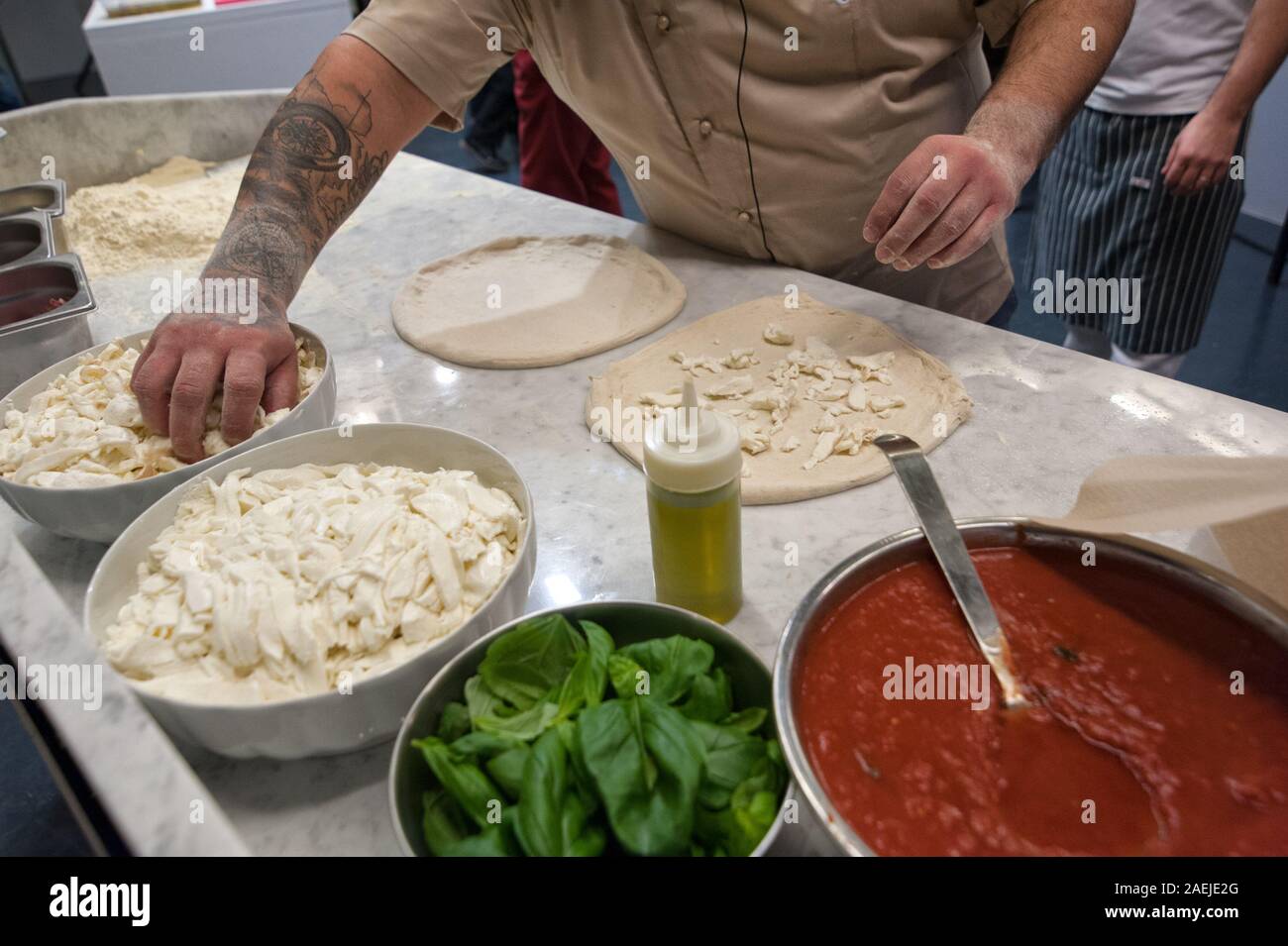 Preparare la Pizza Margherita su un piano di marmo. Pizzaiolo mette i pezzi di mozzarella su un grezzo di impasto per pizza. Foto Stock