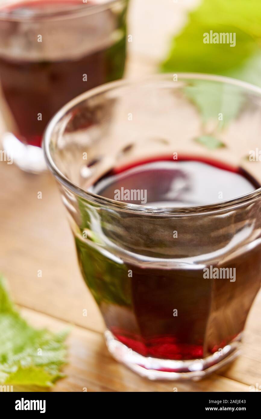 Informale due bicchieri di vino senza il piede e riempita con il vino rosso su una tavola e uva verde foglie. Colpo verticale con il fuoco selettivo. Foto Stock
