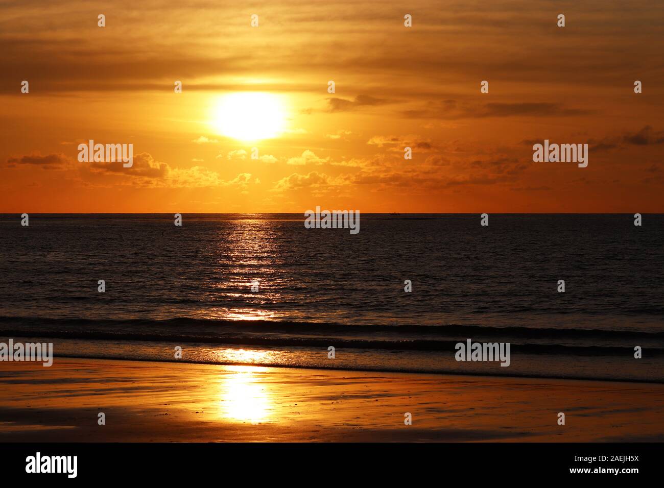 Tramonto su di una spiaggia di sabbia, serata mare, sfondo arancione Sun è riflessa nel drammatico le onde del mare. Acqua scura e nuvole all'orizzonte Foto Stock
