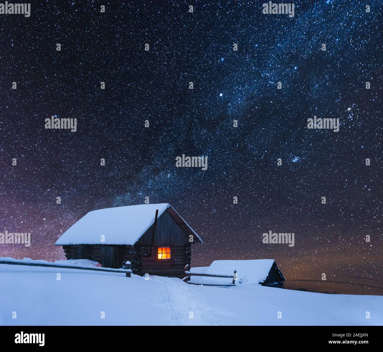 Drammatica scena invernale con casa innevato con una luce calda nella finestra . Fantastico paesaggio notturno incandescente dalla via lattea. In inverno le montagne dei Carpazi, Ucraina, Europa Foto Stock