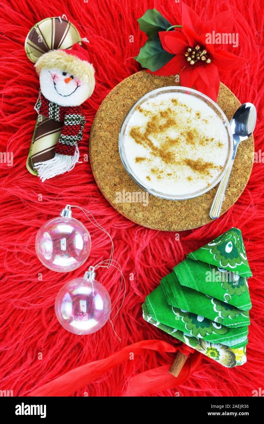 Natale palle trasparenti, un pupazzo di neve faccia,un fiore poinsettia ,budino di riso con cucchiaio e un tovagliolo piegato nella forma di un albero di Natale sul red l Foto Stock