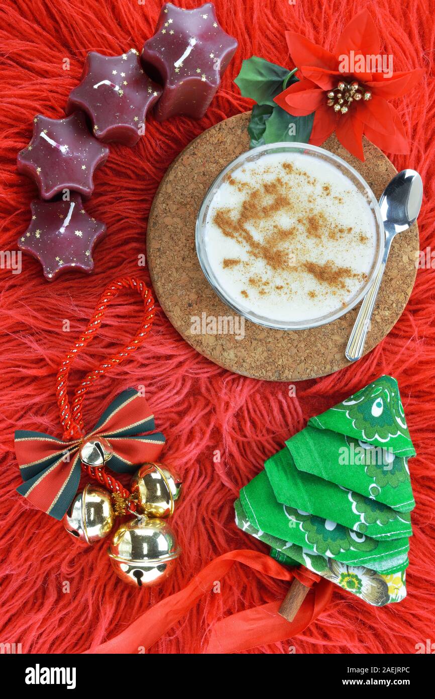 A forma di stella di candele, un fiore poinsettia, natale campane, budino di riso con cucchiaio e un tovagliolo piegato nella forma di un albero di Natale sul rosso ha lunga Foto Stock