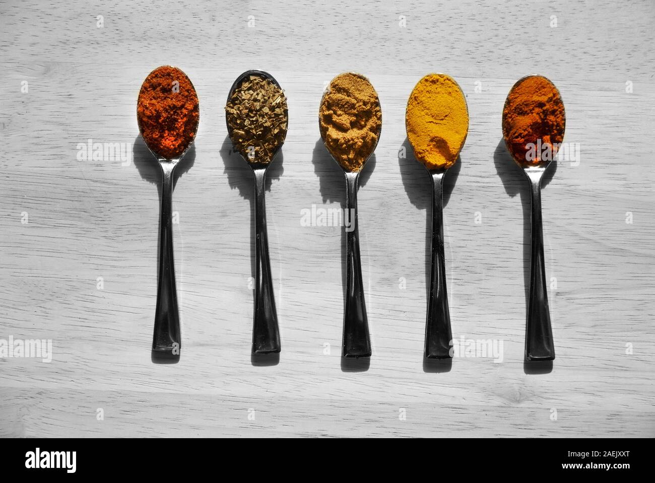 RAINBOW SAPORE: Mini cucchiai con spezie colorate giaceva su un bianco e nero tela di legno. Foto Stock