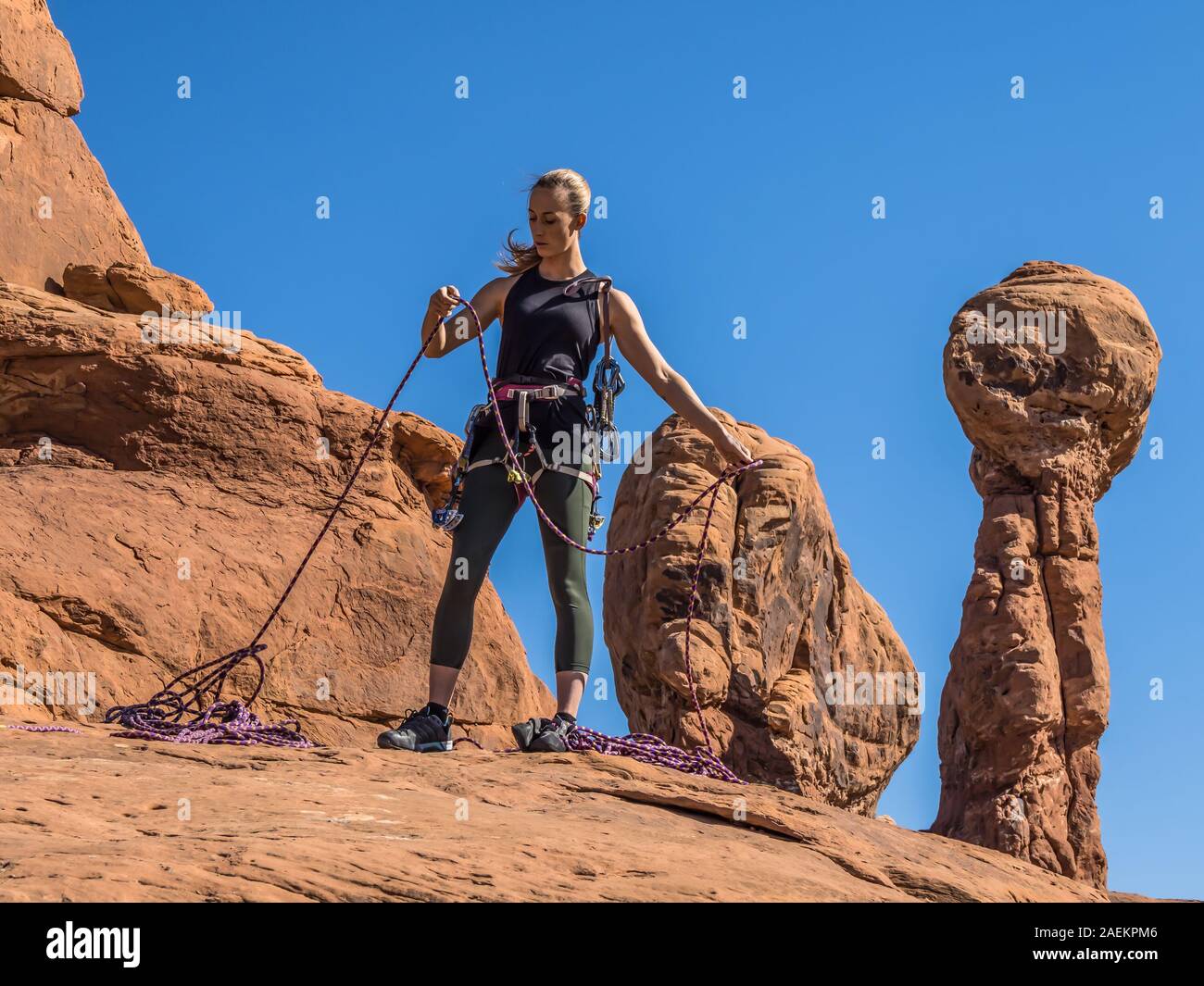 Un attraente giovane donna si prepara per una arrampicata nel giardino di Eden nel Parco Nazionale di Arches nei pressi di Moab, Utah. Foto Stock