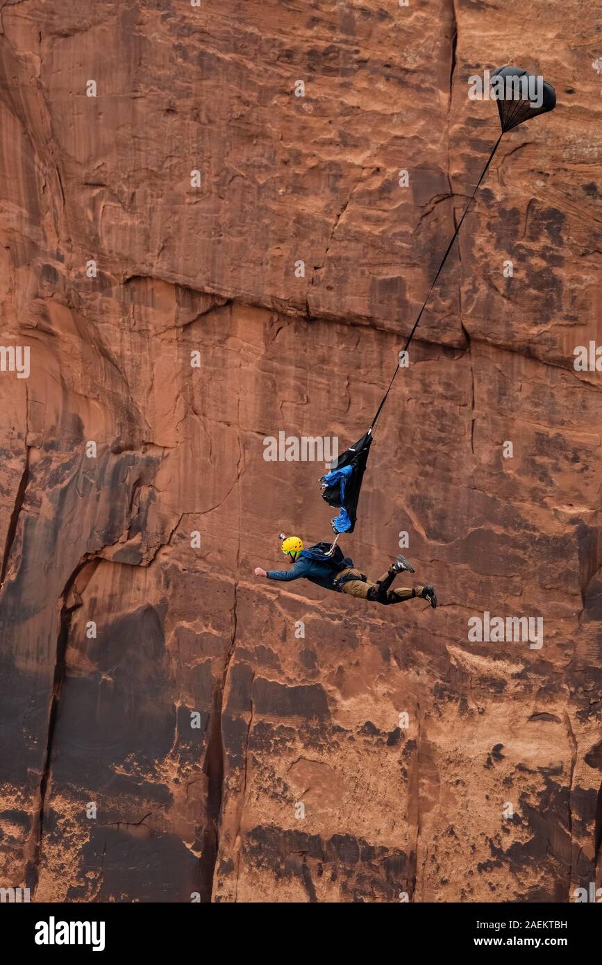 Un ponticello di base libera-cade da una scogliera 950 piedi verticali sopra il piano della valle al Canyon di minerali nei pressi di Moab, Utah. Il suo scivolo pilota ha distribuito Foto Stock