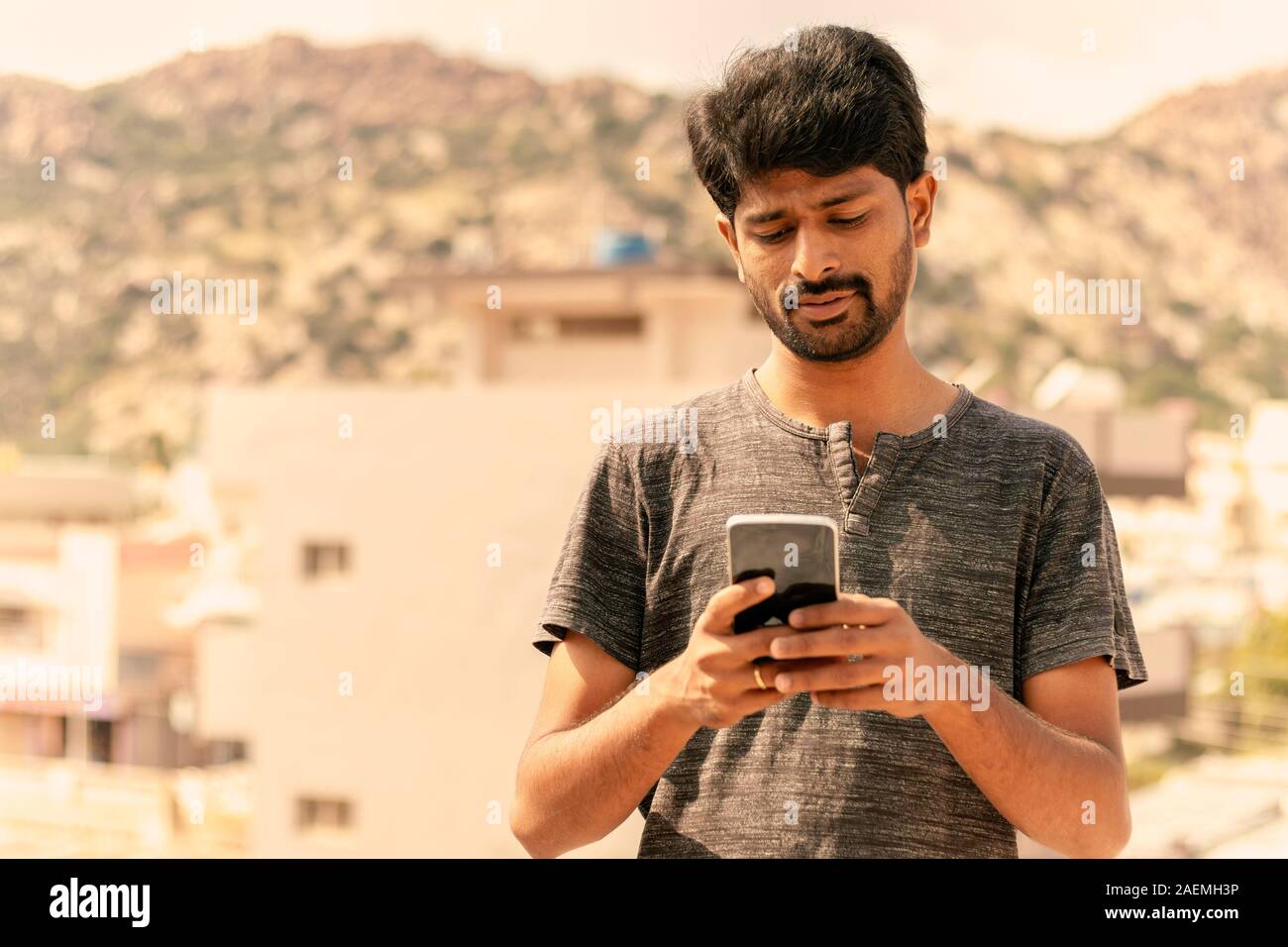 Giovane uomo informale occupato in utilizzando una smart phone texting messaggi sulla terrazza. Foto Stock