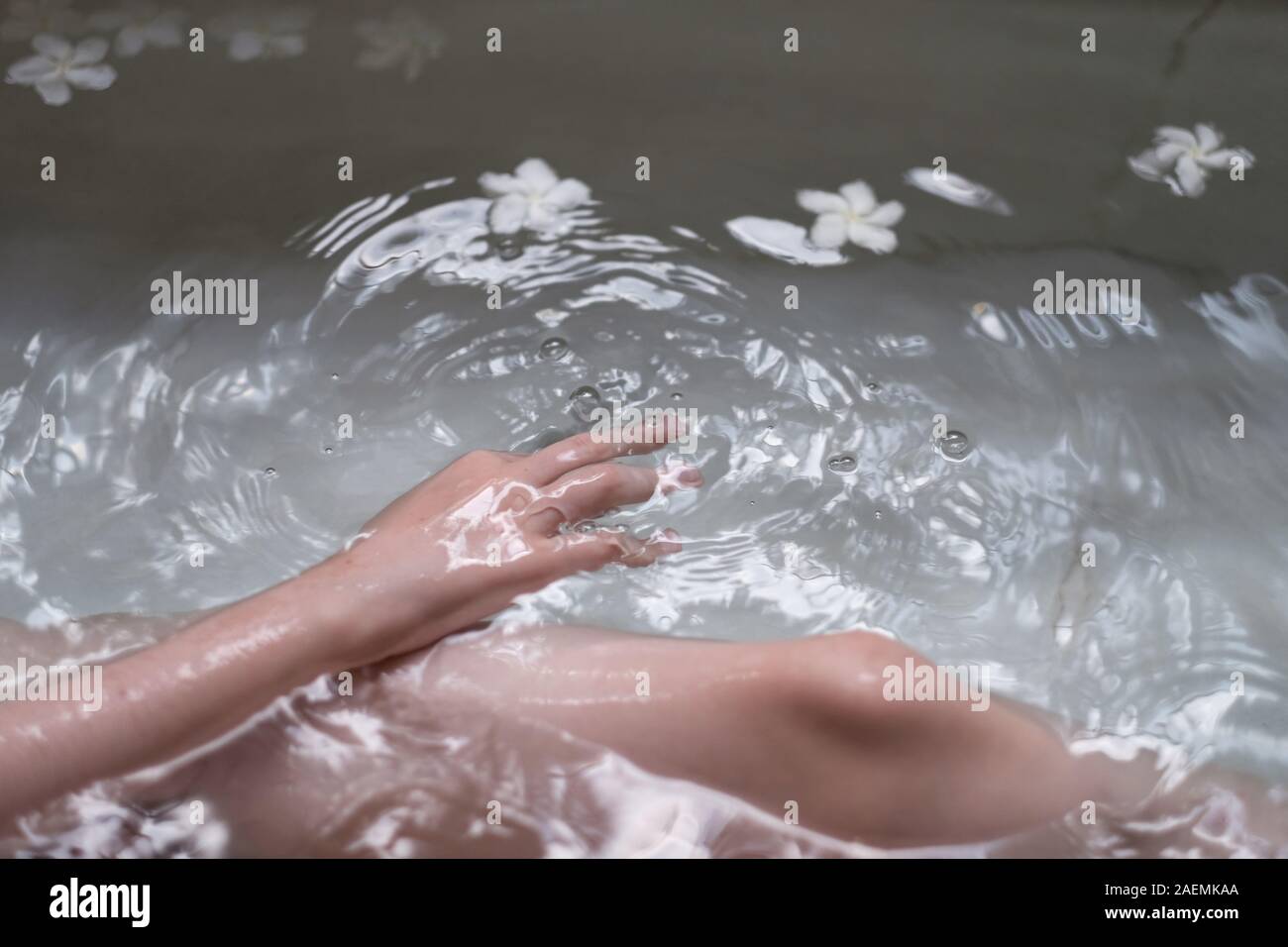 Il bambino si trova in una vasca con acqua e petali di fiori bianchi Foto Stock Il bambino si trova in una vasca con acqua e petali di fiori bianchi Foto Stock