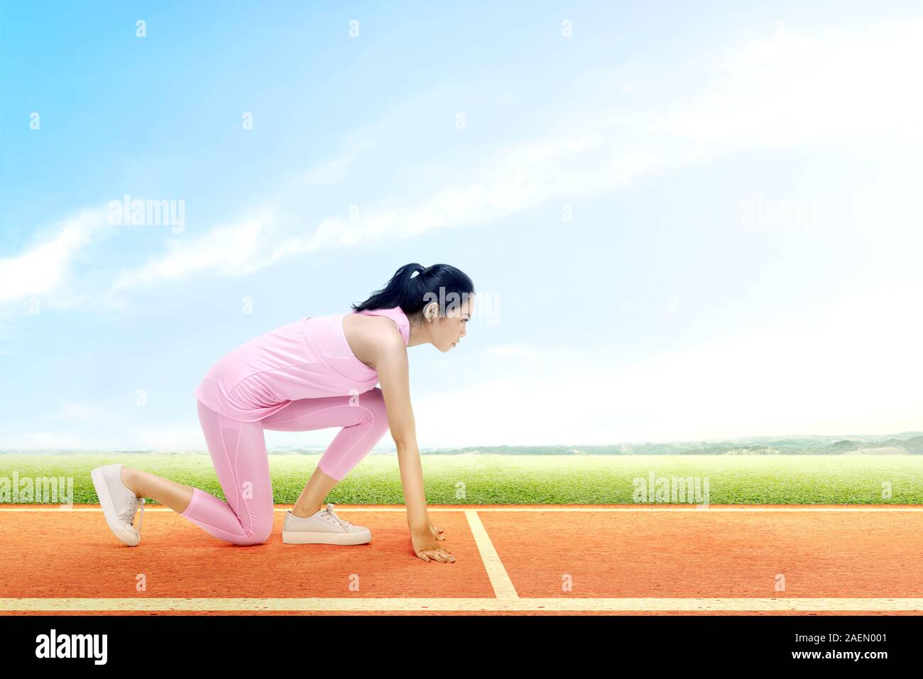 Asian runner donna pronto a correre sulla pista da corsa con un cielo blu sullo sfondo Foto Stock