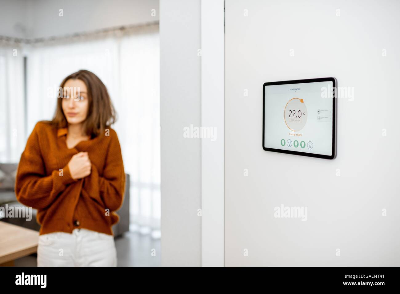 Pannello digitale per la casa intelligente gestione con lanciato riscaldamento Applicazione di controllo nel soggiorno. Donna sensazione di freddo sullo sfondo Foto Stock