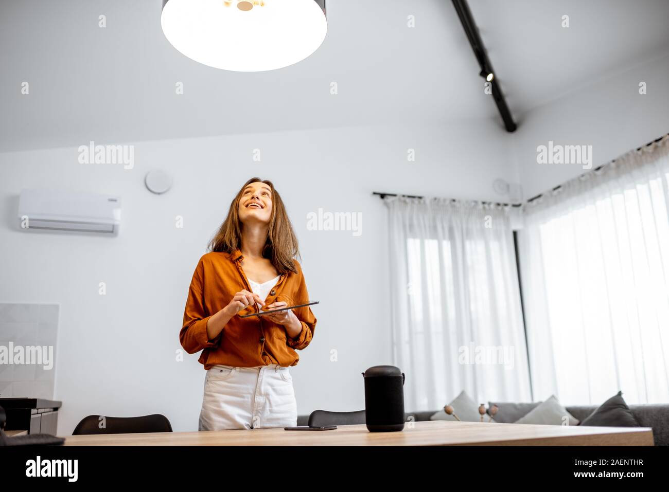 Giovane donna il controllo a casa di luce con dstoccaggio nel BOH degli Smart in casa nel salotto. Concetto di una casa intelligente e un controllo della luce con i dispositivi mobili Foto Stock