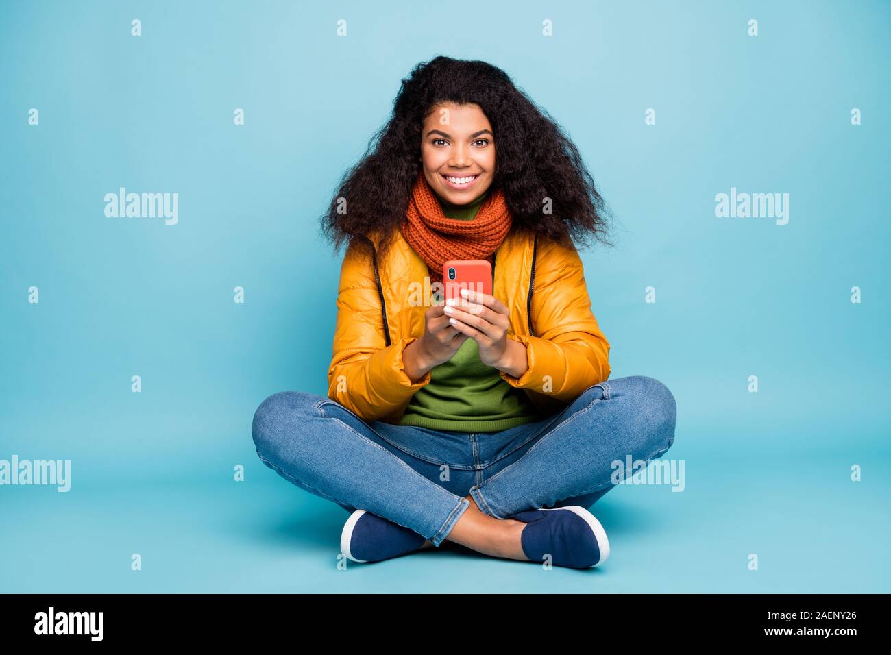 Foto di divertenti pelle scura signora azienda telefono mani seguaci di controllo piano di seduta gambe incrociate di usura della molla gialla soprabito jeans maglione sciarpa Foto Stock