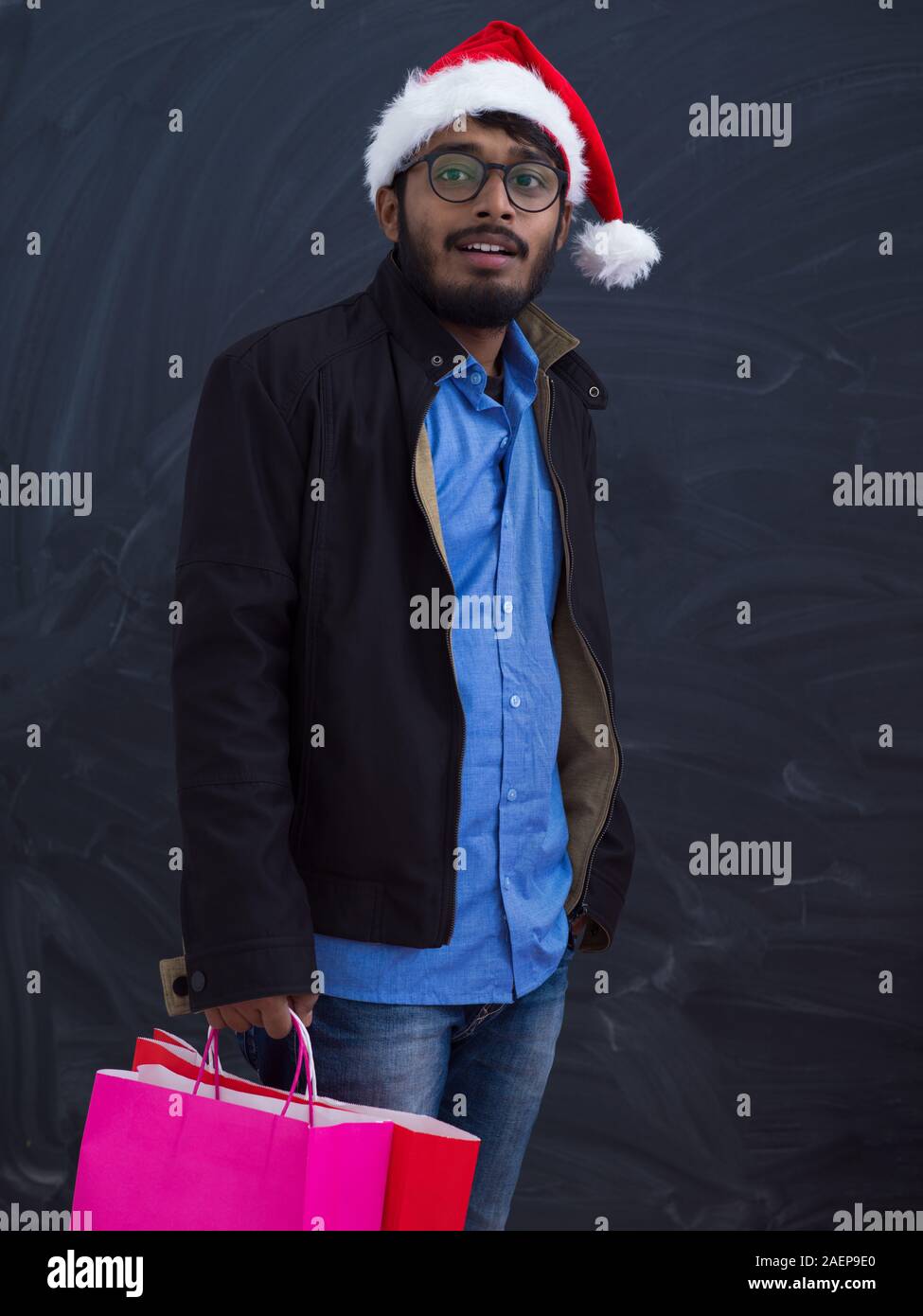 Indian uomo che indossa abiti di festa di Santa hat con shopping bag su sfondo scuro studio dark scuoiati Middle Eastern Santa Claus Buon Natale Foto Stock