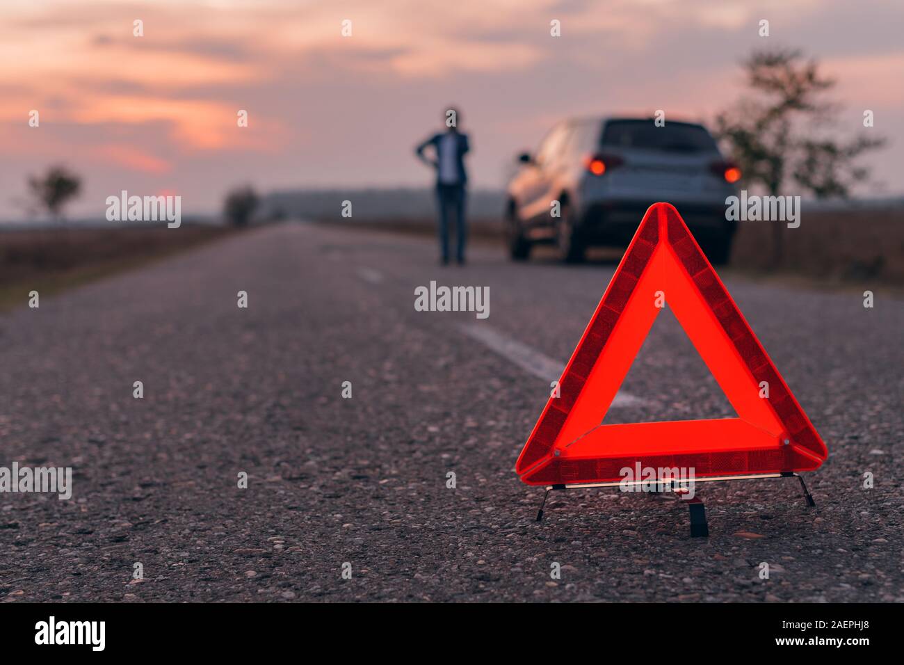 Il triangolo di avvertenza segno sulla strada, donna in blur sullo sfondo per chiedere assistenza stradale dalla Broken auto, il fuoco selettivo Foto Stock