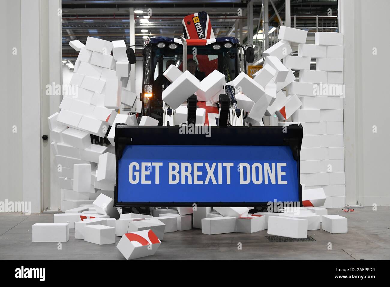 Il primo ministro Boris Johnson aziona una bandiera europea-tema JCB, con le parole 'Get Brexit fatto' all'interno della benna di scavo, attraverso un muro falso blasonate con la parola 'Gridlock', durante una visita a JCB cabina centro di fabbricazione in Uttoxeter, durante la campagna elettorale del trail. Foto Stock