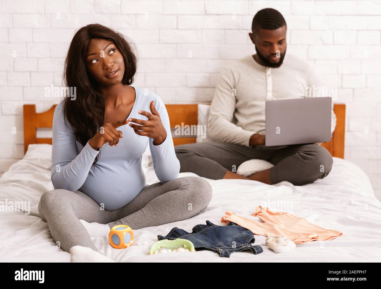 Bella donna incinta la preparazione di vestiti del bambino, marito utilizzando laptop Foto Stock