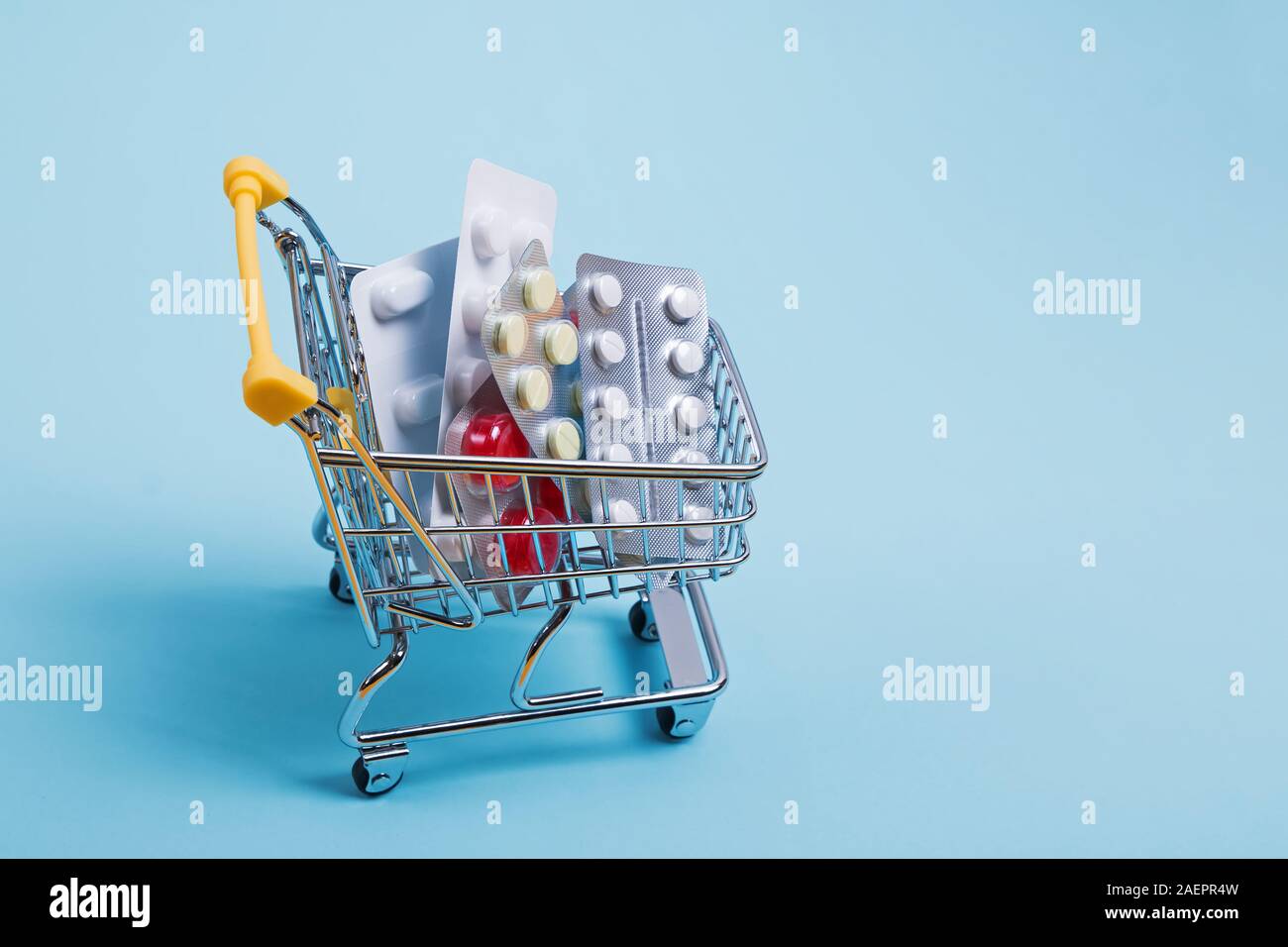 Miniatura carrello della spesa pieno di pillole su sfondo blu. Foto Stock