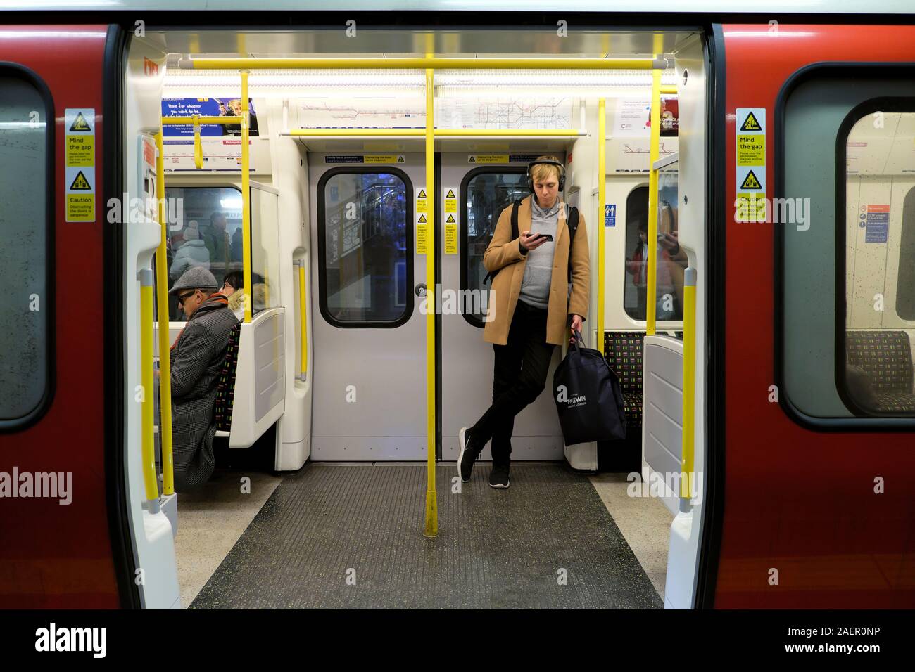 Giovane uomo in piedi in treno sotterraneo carrello con le porte aperte in attesa su una stazione della metropolitana platform guardando il telefono cellulare Londra UK KATHY DEWITT Foto Stock