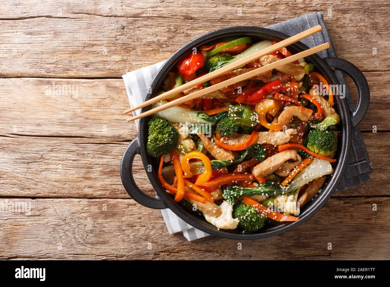 Cucina cinese rosolare la carne di maiale con verdure e semi di sesamo close-up in una padella sul tavolo. Parte superiore orizzontale vista da sopra Foto Stock