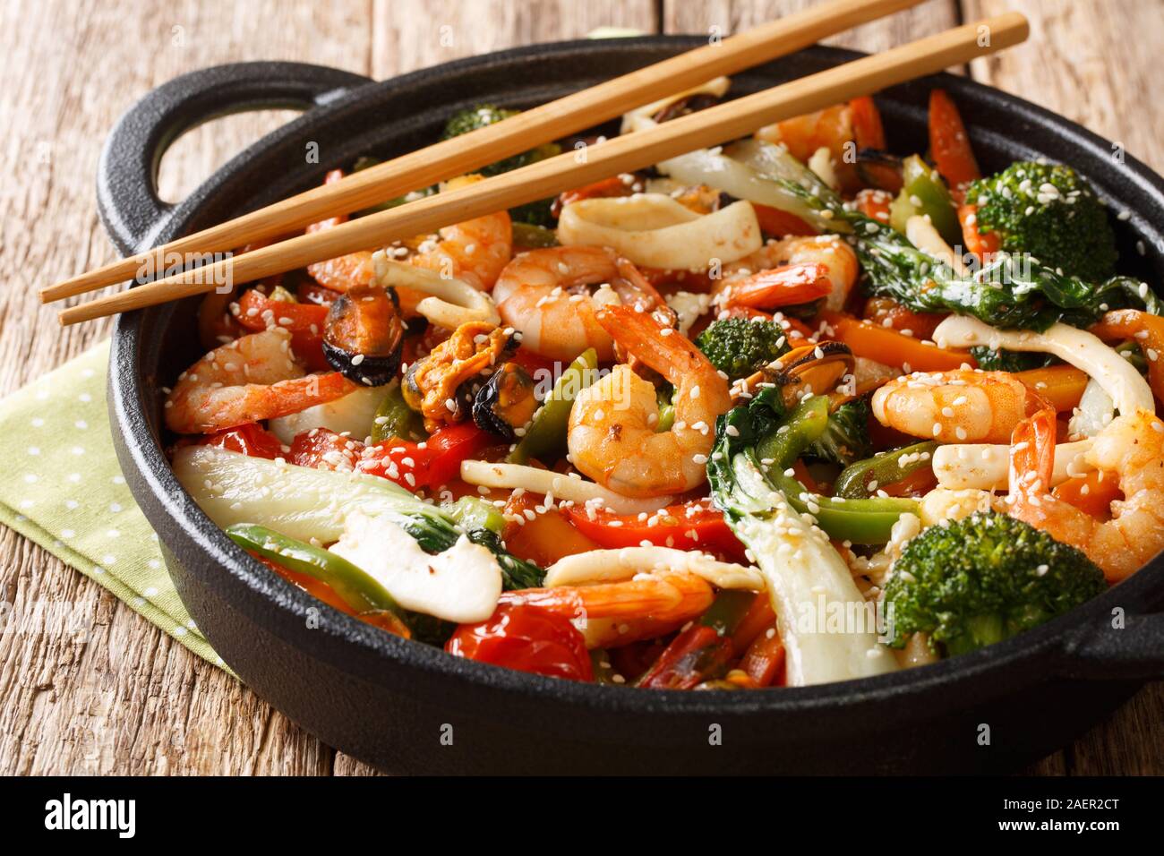 Una pentola mescolare gamberi fritti, calamari e cozze con fresche verdure di stagione di close-up in una padella sul tavolo orizzontale. Foto Stock