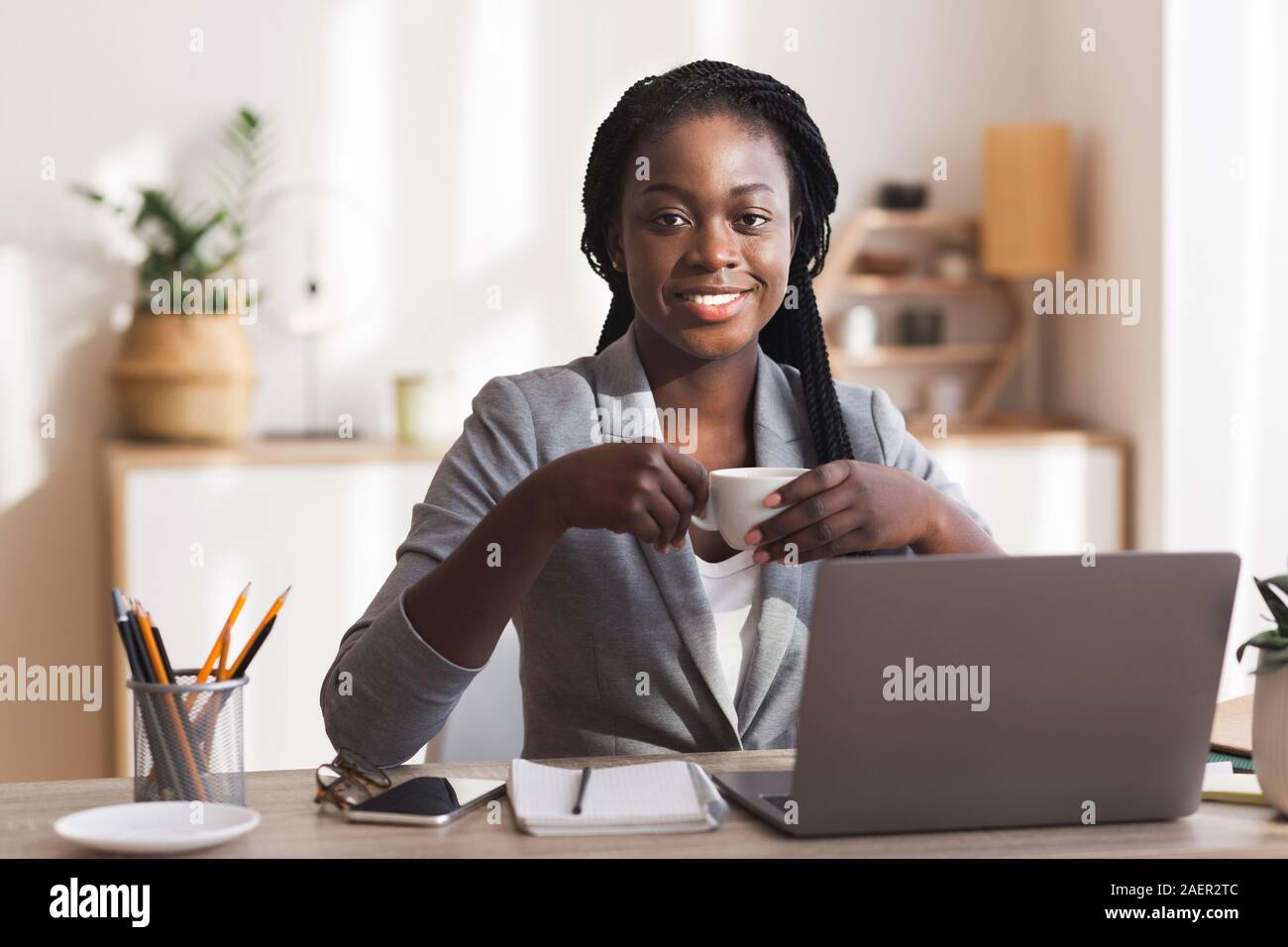 Sorridente African American segretario di bere il caffè al posto di lavoro in un ufficio moderno Foto Stock