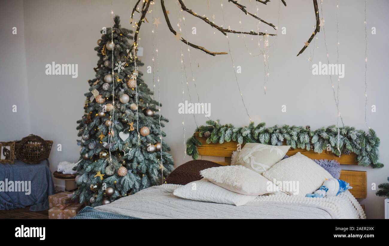 Romantica camera da letto in colori luminosi e con molte ghirlande, un albero di Natale decorato con legno, legno e arredamento eco. Natale interno in colori pastello Foto Stock