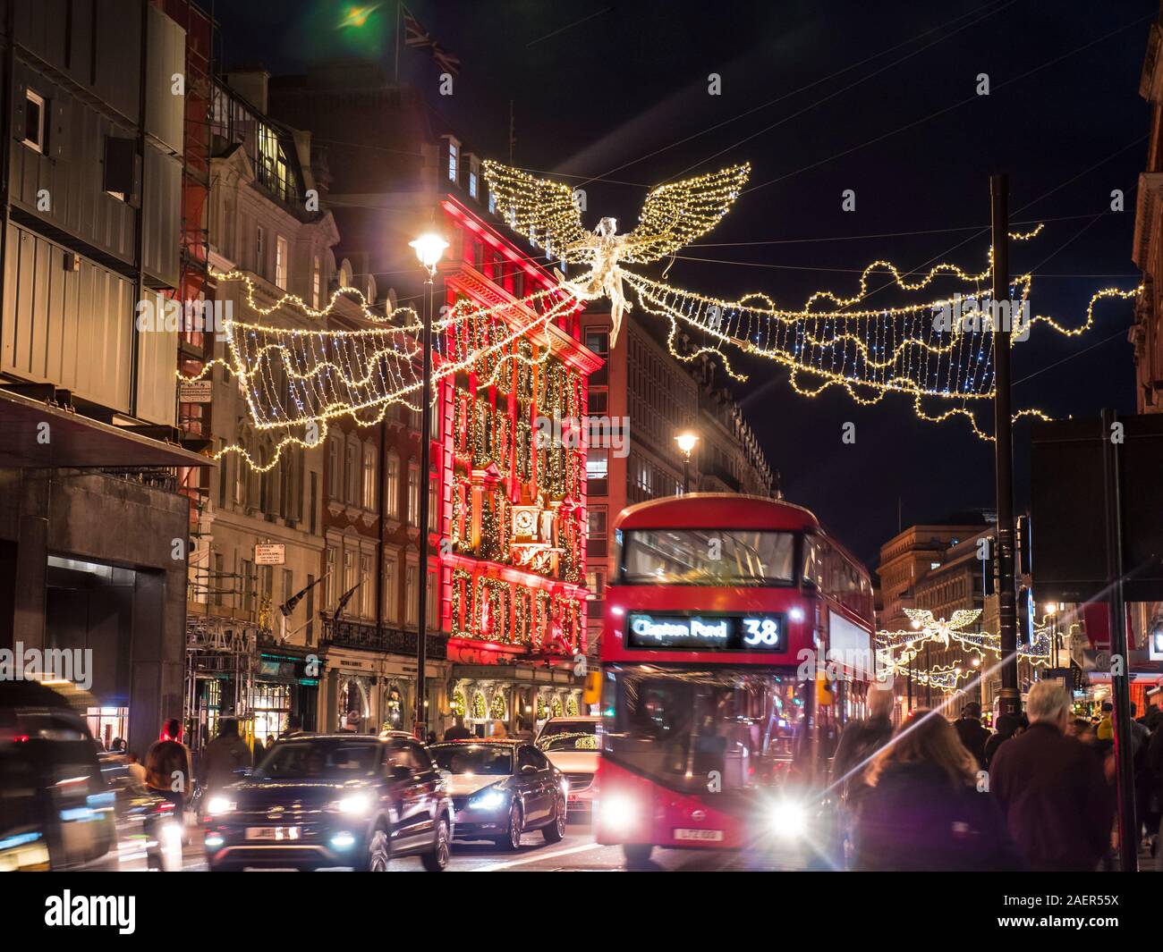 Natale Piccadilly di notte con Fortnum e Mason Store illuminato con calendario dell'Avvento il tema e il red hybrid London bus, acquirenti e il traffico con il Natale Golden Angel luminarie di luci di Piccadilly London REGNO UNITO Foto Stock