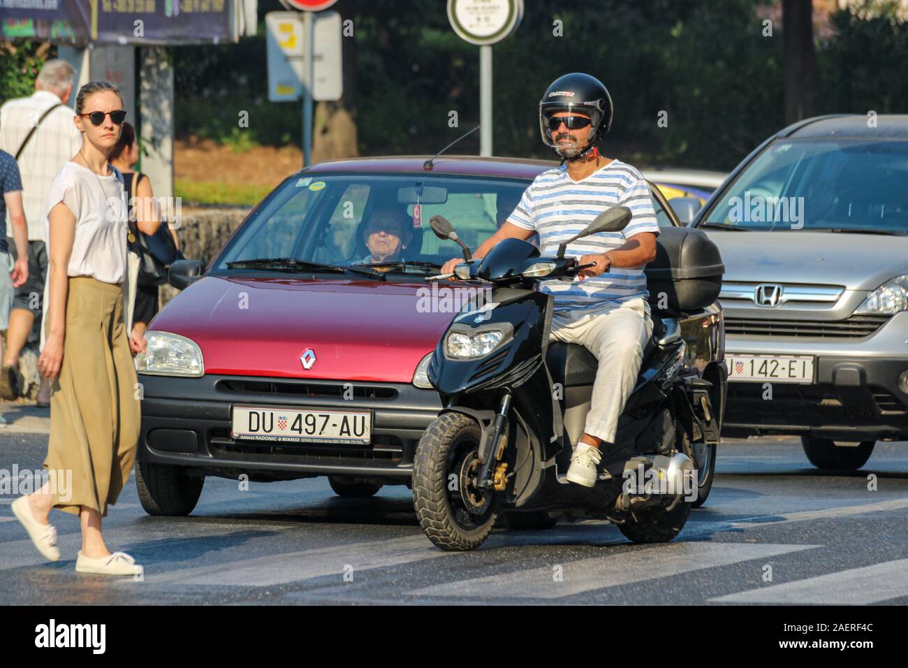 Auto e moto scooter in attesa dalla zebra attraversamento pedonale mentre attraversa la strada a Dubrovnik, Croazia Foto Stock