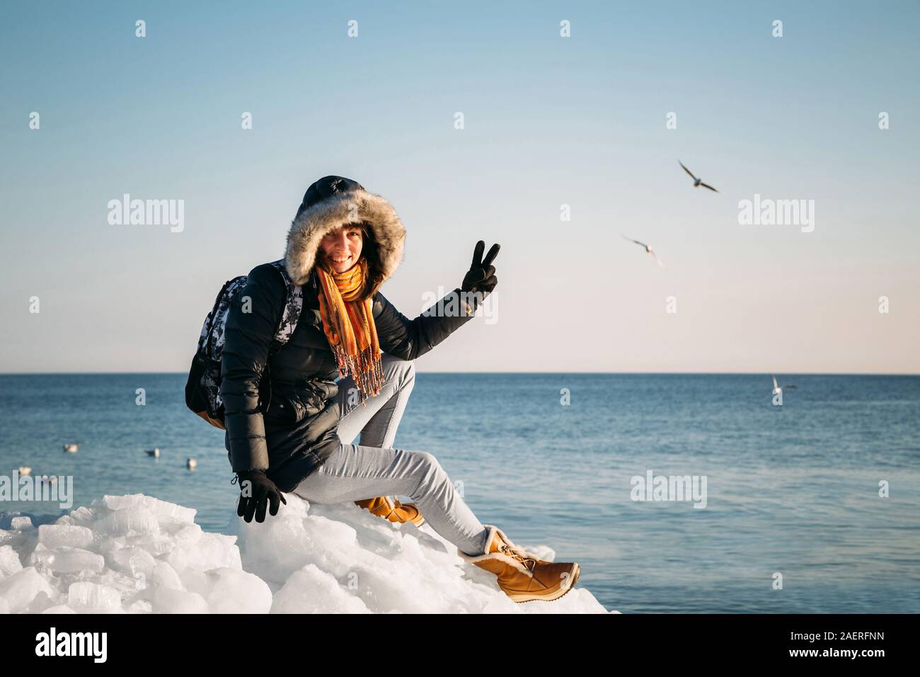 Giovane donna sorridente seduto sulla cima del mare i blocchi di ghiaccio sulla costa azienda rotto pezzo di ghiaccio, con il blu del mare e del cielo e lo sfondo Foto Stock