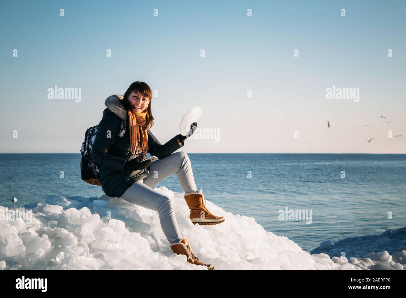 Giovane donna sorridente seduto sulla cima del mare i blocchi di ghiaccio sulla costa azienda rotto pezzo di ghiaccio, con il blu del mare e del cielo e lo sfondo Foto Stock