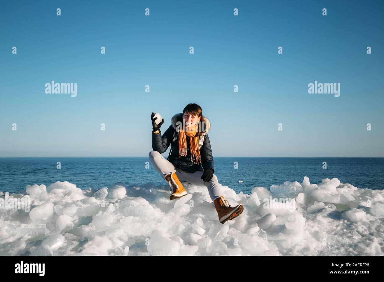 Giovane donna sorridente seduto sulla cima del mare i blocchi di ghiaccio sulla costa azienda rotto pezzo di ghiaccio, con il blu del mare e del cielo e lo sfondo Foto Stock
