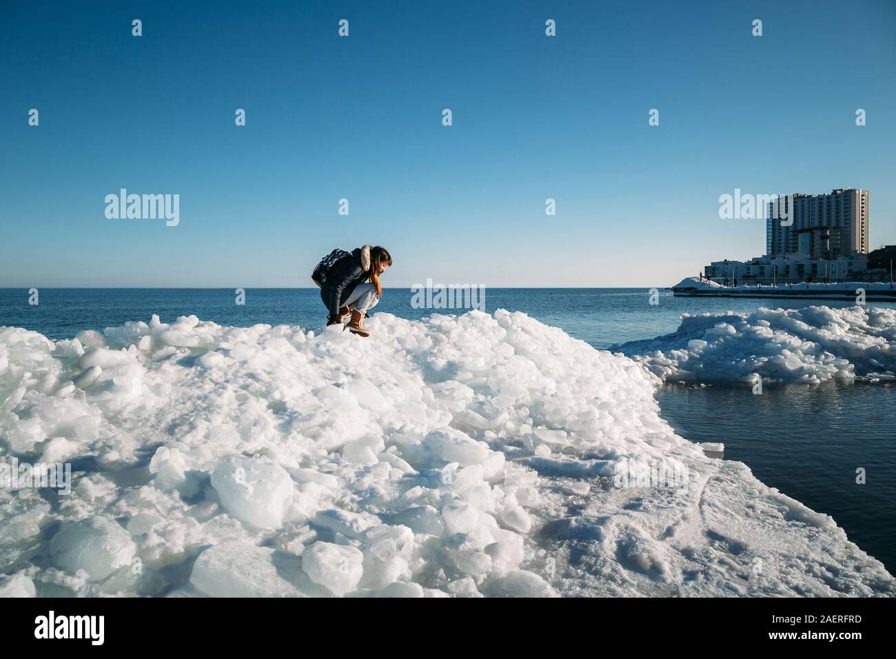 Giovane donna sorridente seduto sulla cima del mare i blocchi di ghiaccio sulla costa azienda rotto pezzo di ghiaccio, con il blu del mare e del cielo e lo sfondo Foto Stock