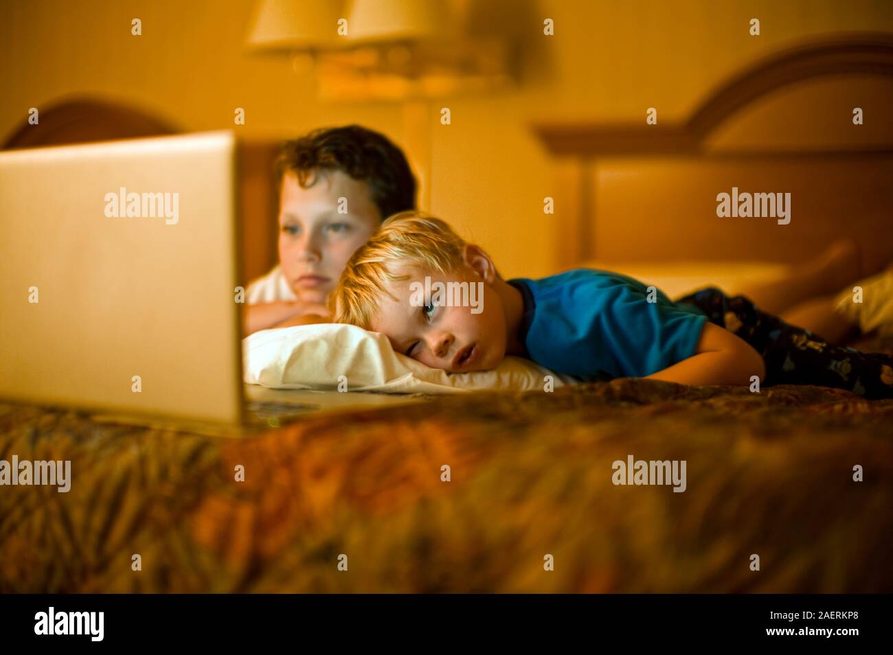 Un ragazzo e il suo fratello più giovane guarda un laptop con schermo anteriore giacente in giù su un letto insieme. Foto Stock