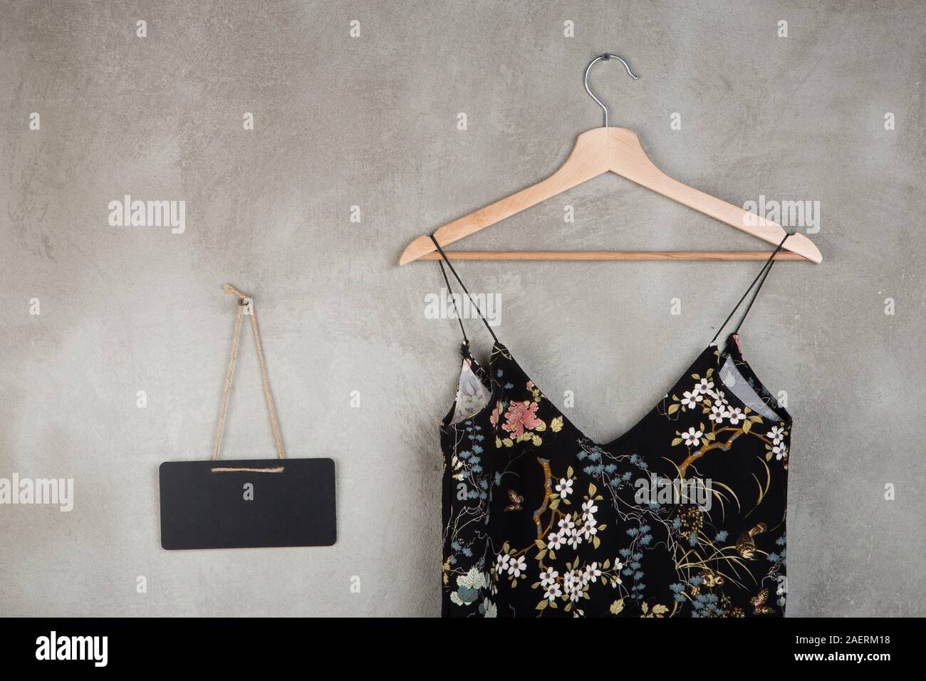 La moda e lo shopping concetto - lavagna vuota e bellissima little black dress in motivo floreale su un appendiabiti su sfondo grigio Foto Stock