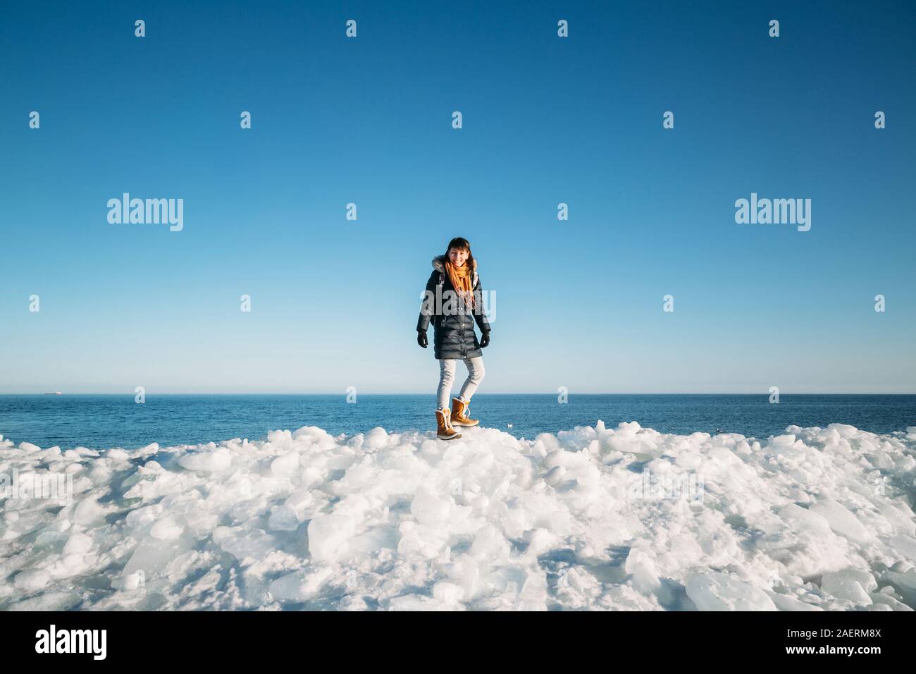 Giovane donna sorridente in piedi sulla parte superiore del mare i blocchi di ghiaccio sulla costa con il blu del mare e del cielo e lo sfondo Foto Stock