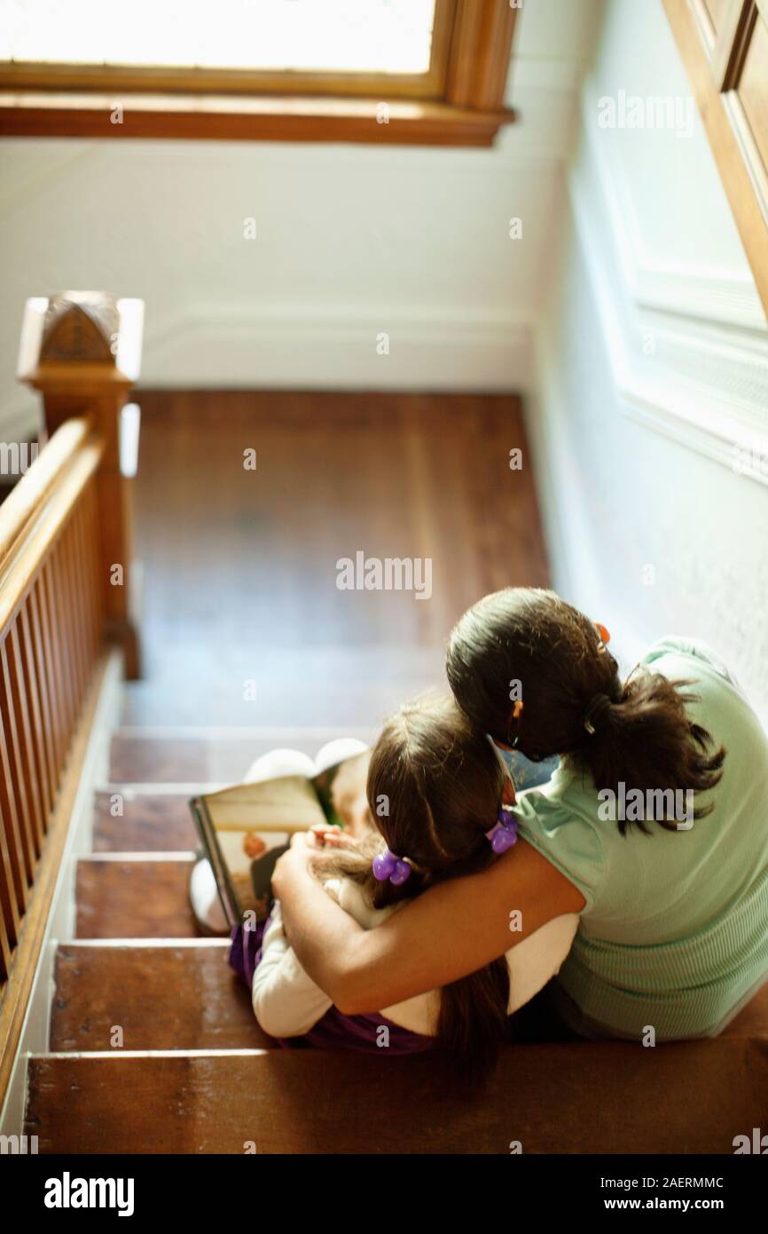 La donna e la sua giovane figlia a sedersi su una rampa di scale di lettura di un libro. Foto Stock