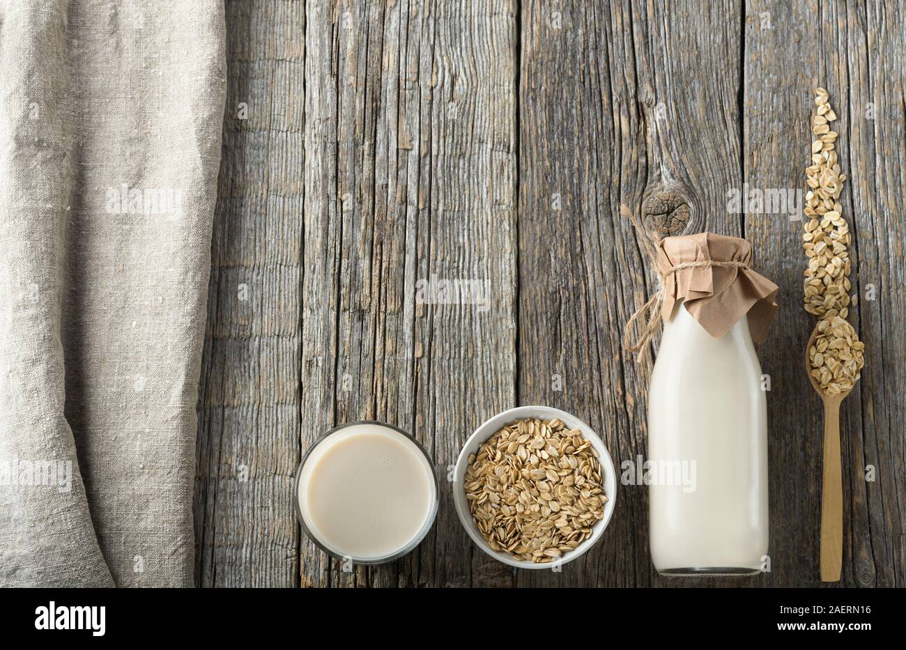Latte di avena in una bottiglia e in un bicchiere su un tavolo di legno. Latte e ingredienti laici piana. Senza latte e derivati del latte prodotto.Immagine con spazio copia,verticale. Foto Stock