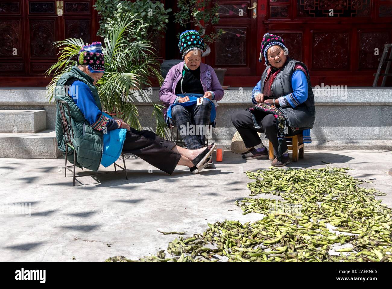 Marzo 14, 2019: etnico donne anziane la cucitura in un cortile con un sacco di baccelli sul terreno, Xizhou, Yunnan, Cina Foto Stock